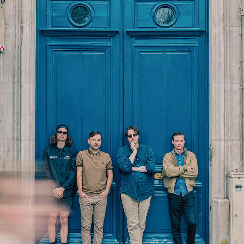 photo promotionnelle des quatre musiciens devant une grande porte d'immeuble bleue
